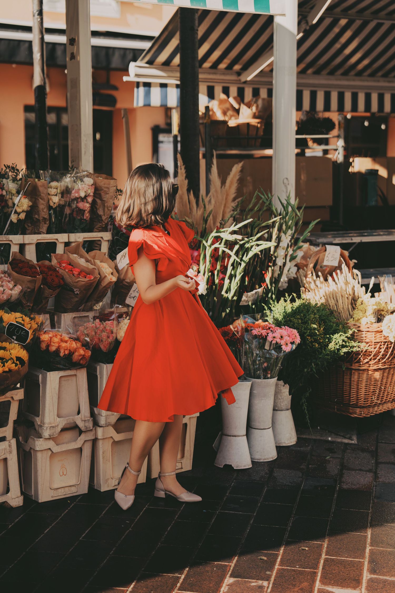 Woman in red dress browsing colorful flowers at an outdoor market stall.