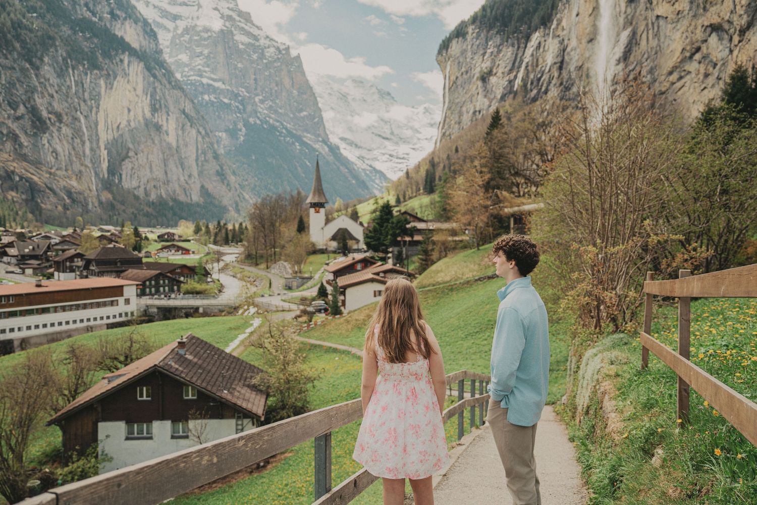Teenage siblings walking on a path overlooking the scenic Lauterbrunnen village and waterfall in Switzerland.