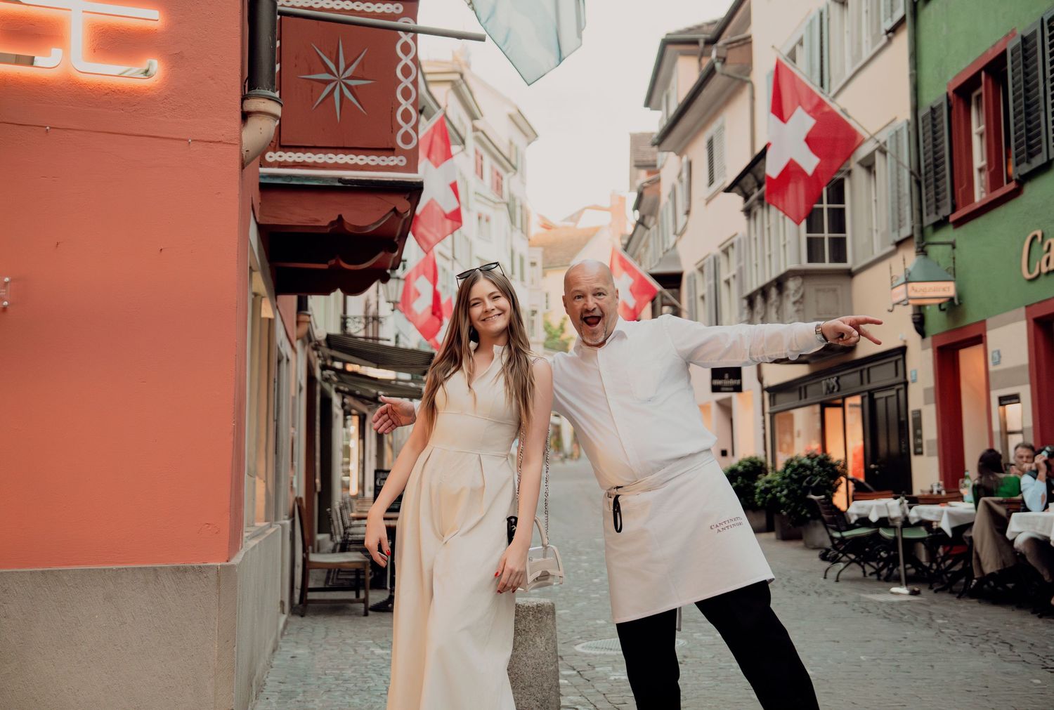 Cheerful couple waving Swiss flags on colorful cobblestone street in old town Zurich, Switzerland.
