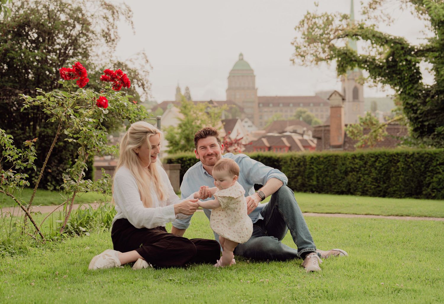 Young family with baby sitting on grass with a historic domed building in the background.