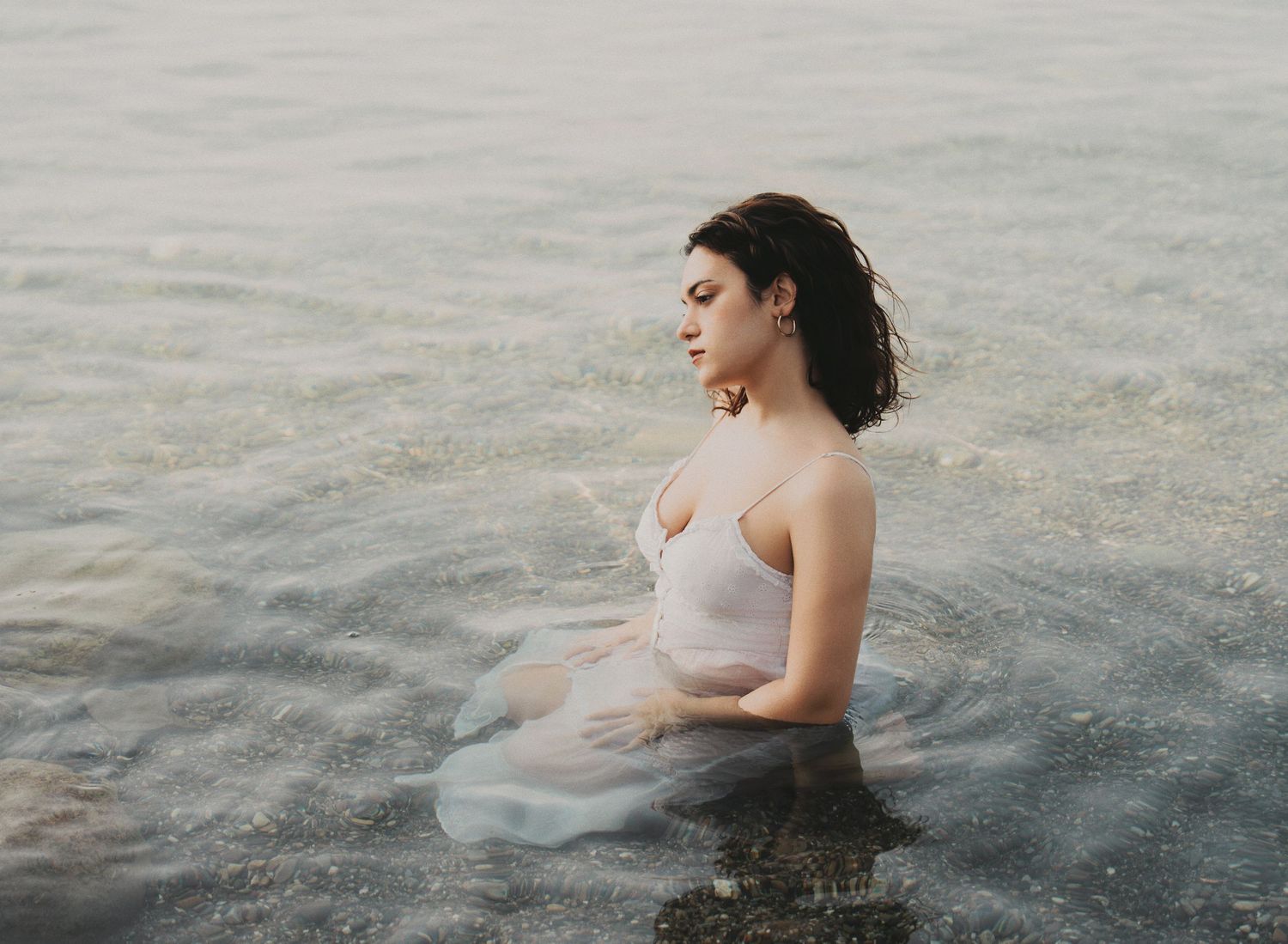Woman in white dress sitting peacefully in calm ocean waters with eyes closed.