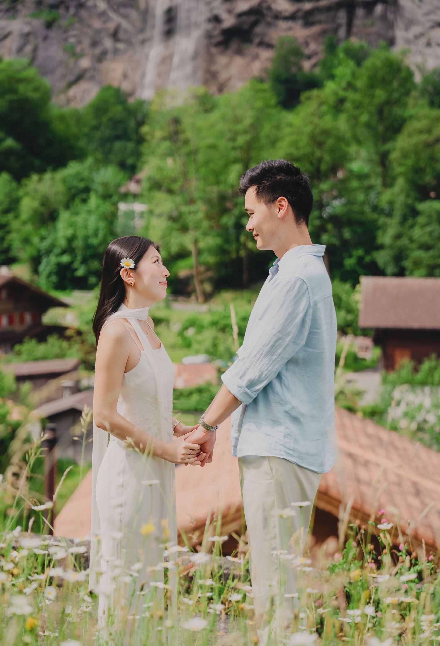 Couple holding hands in a wildflower meadow with a waterfall and Swiss village backdrop in Lauterbrunnen.