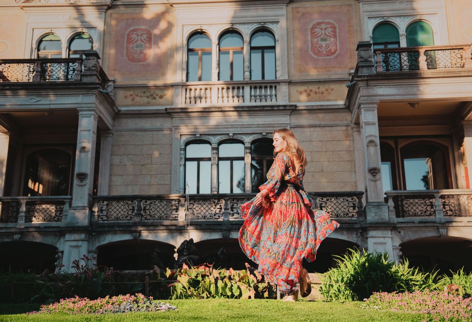 Woman twirls in colorful floral maxi dress in front of a grand ornate historic building facade.