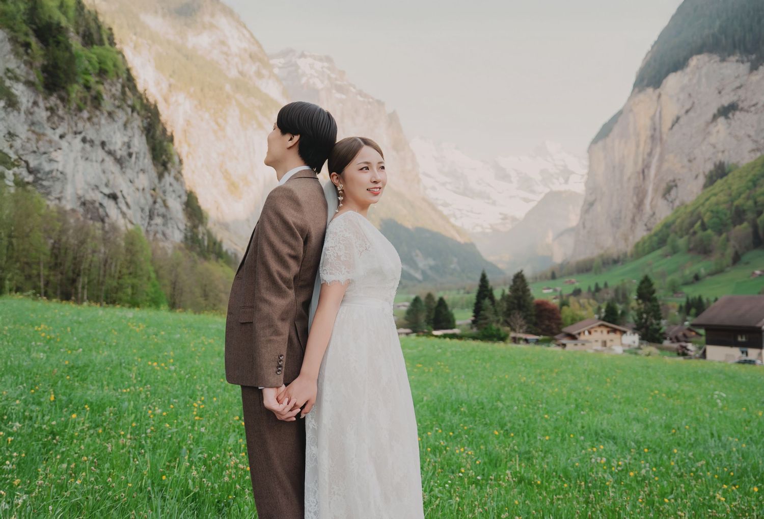 Bride and groom holding hands in a flower-dotted meadow with stunning Lauterbrunnen valley views.