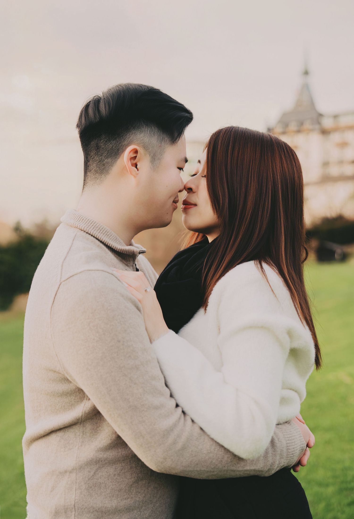 Romantic couple sharing an intimate moment about to kiss in a lush green park with a castle backdrop.