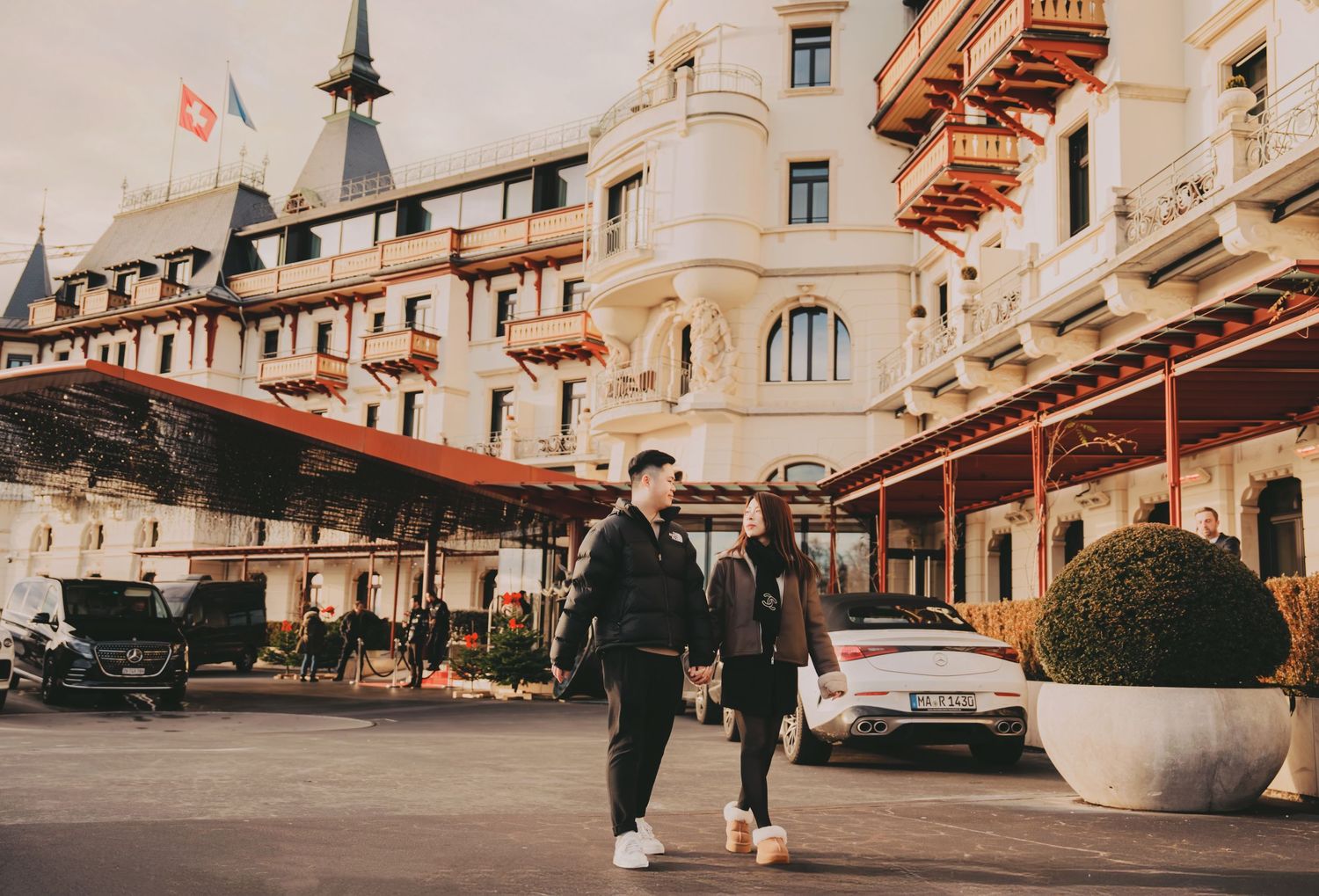Couple walking hand in hand outside a luxurious European grand hotel on a sunny day.