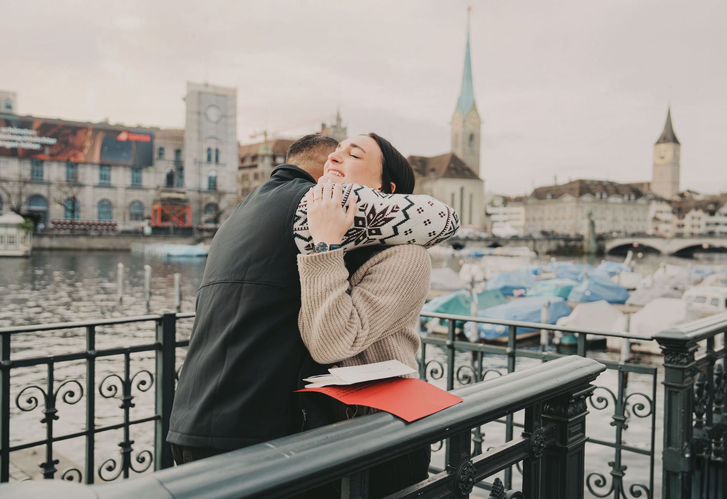 Woman laughing joyfully during romantic moment on Zurich bridge with city skyline backdrop.