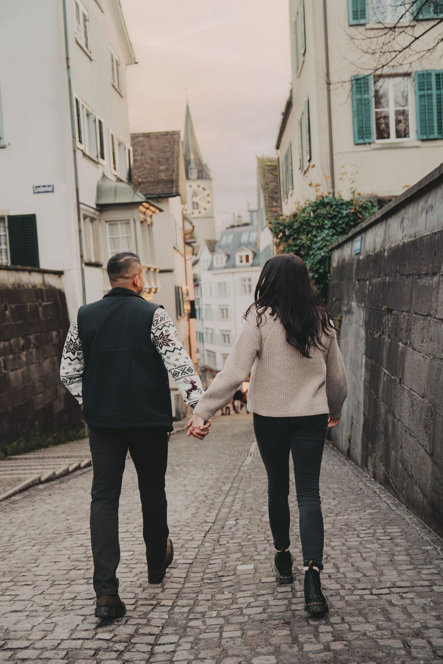 Couple walking away hand-in-hand on a cobblestone street in a European old town.