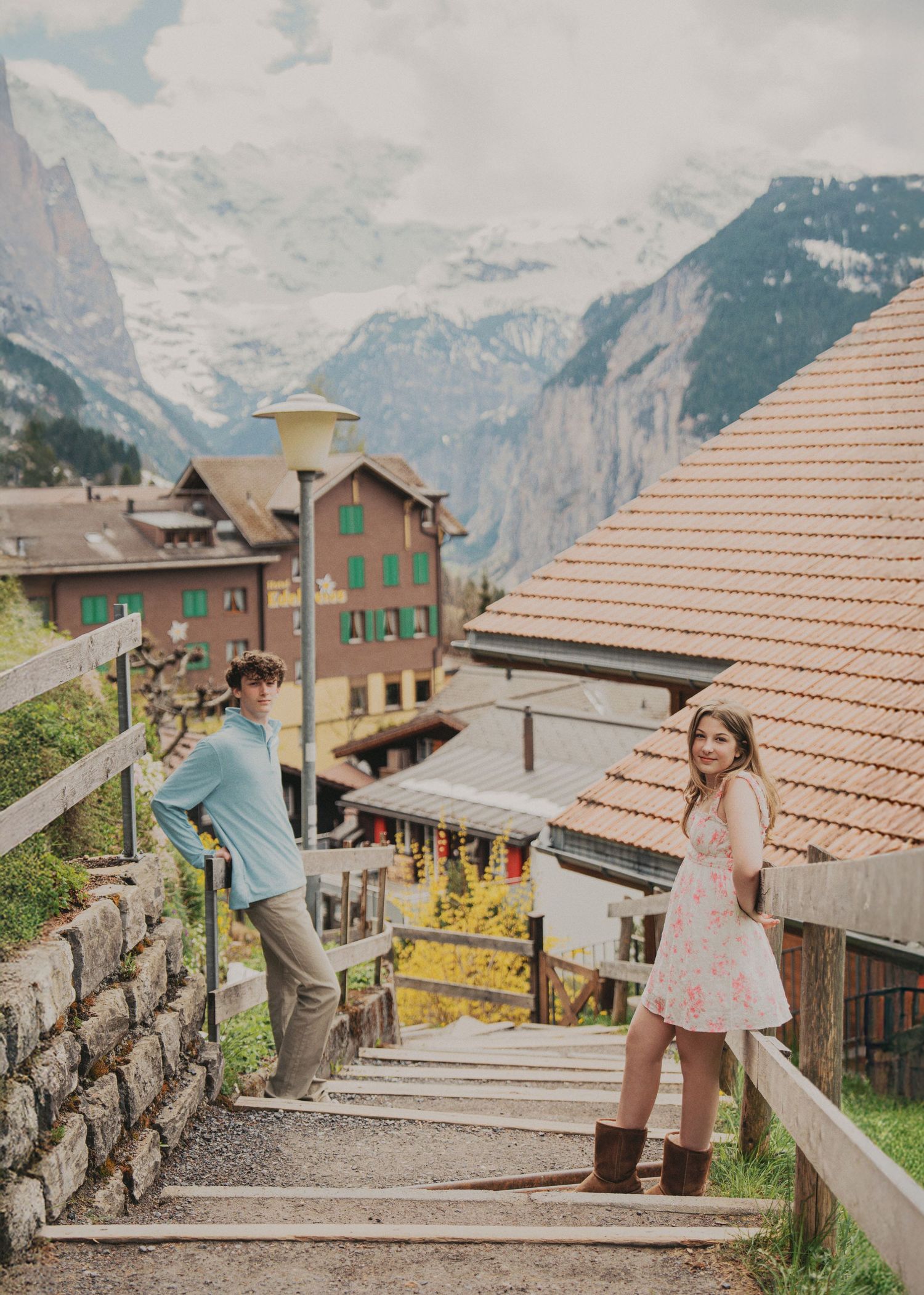 Couple standing on stairs in charming Swiss village with traditional buildings and dramatic Alpine mountains.