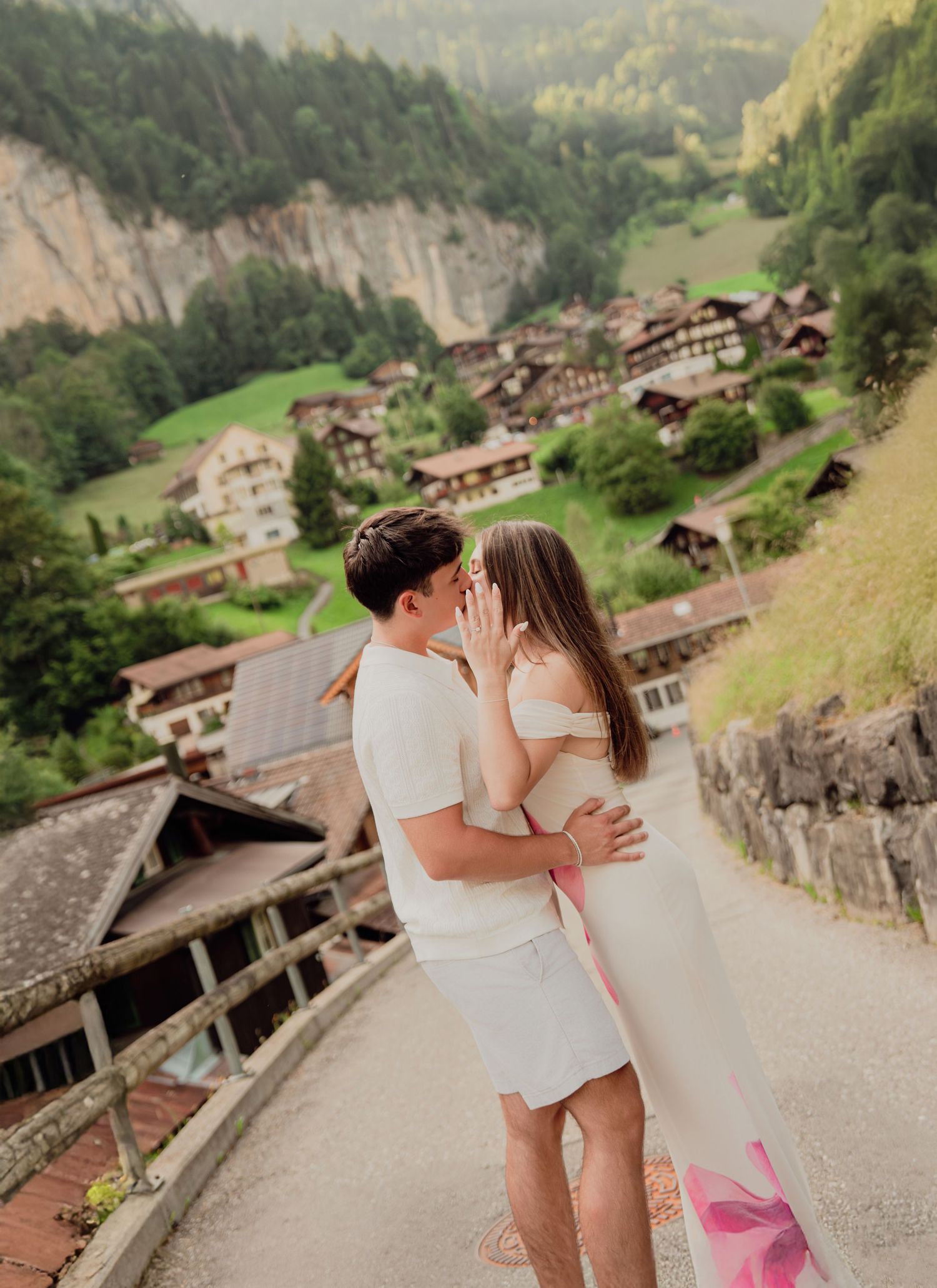 Romantic couple in white outfits kissing on a scenic path overlooking the picturesque Swiss village of Lauterbrunnen.
