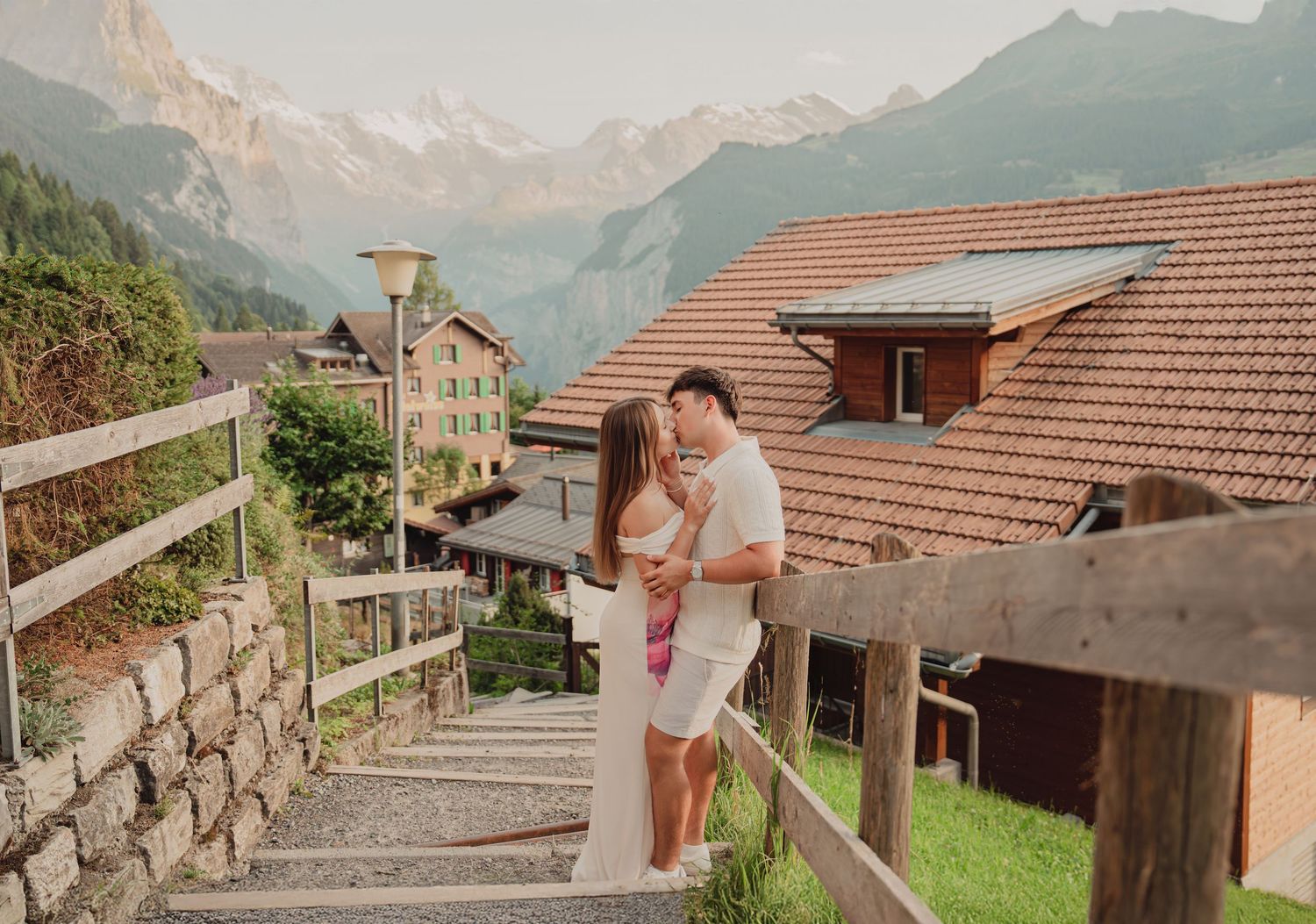 Couple sharing a tender moment on wooden steps in scenic Swiss mountain village with Alps views.