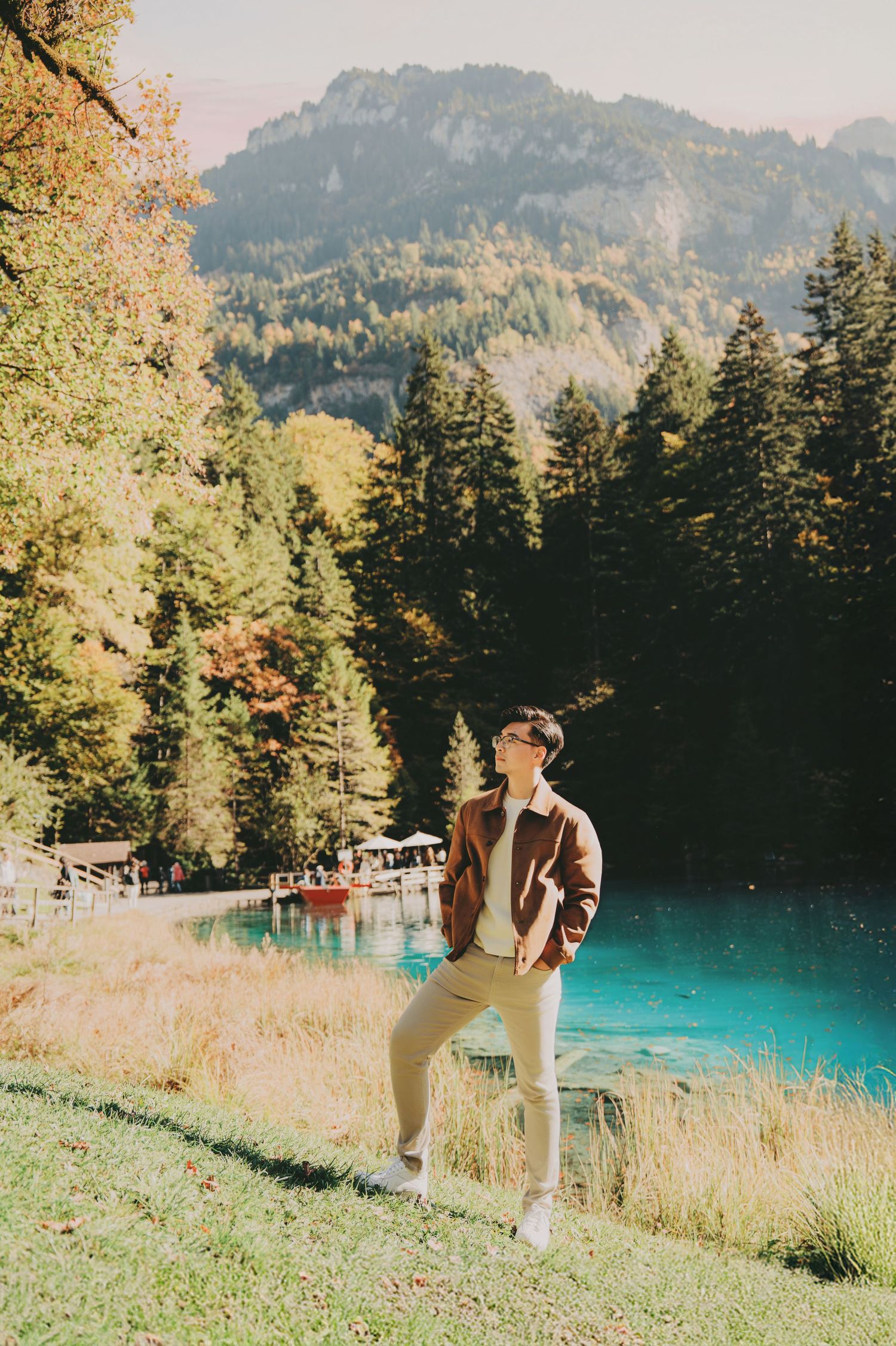 Young man posing by a stunning turquoise mountain lake surrounded by autumn foliage and pine trees.