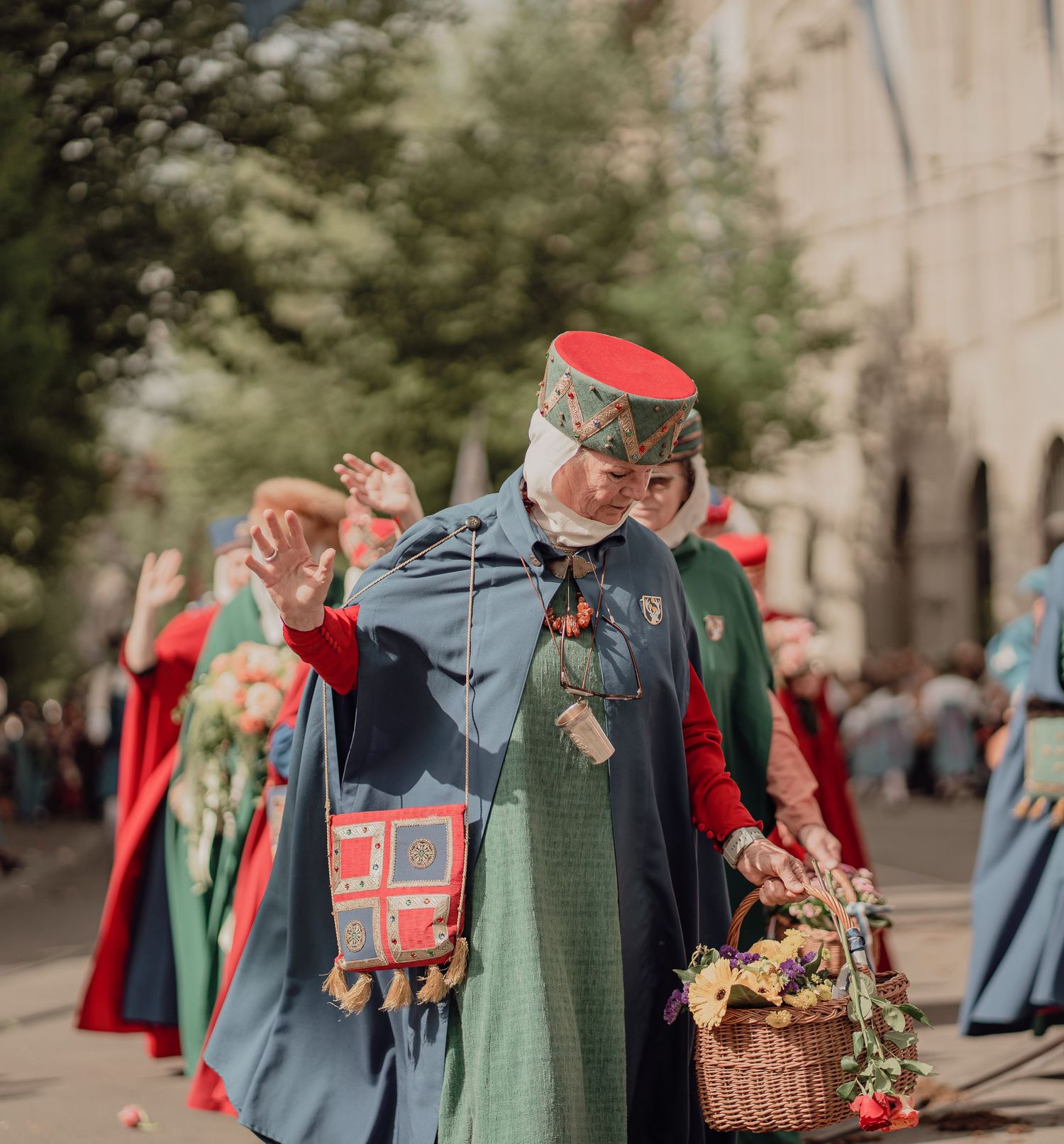 Woman in red and green medieval folk costume carries flower basket during traditional cultural procession.
