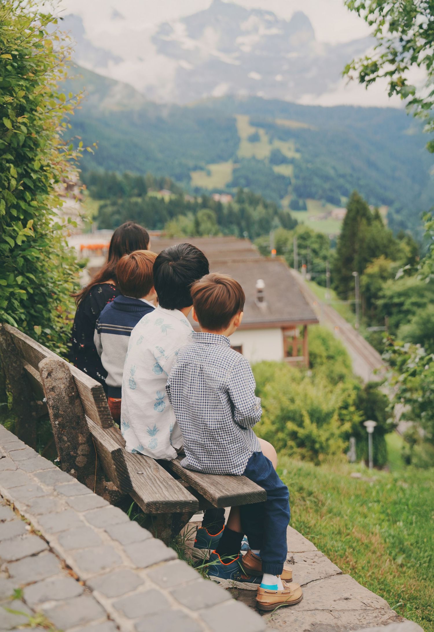 Four children sit closely on a bench enjoying the breathtaking Swiss mountain landscape view.