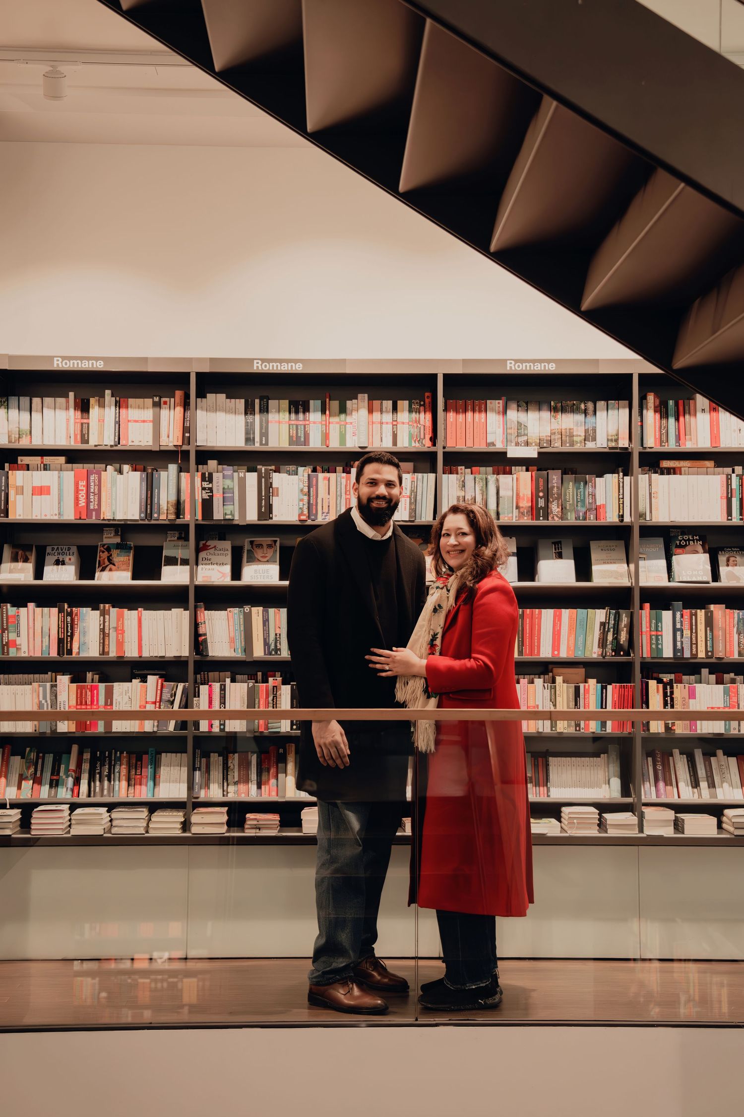 Couple posing together in front of a modern bookstore shelf filled with colorful books.