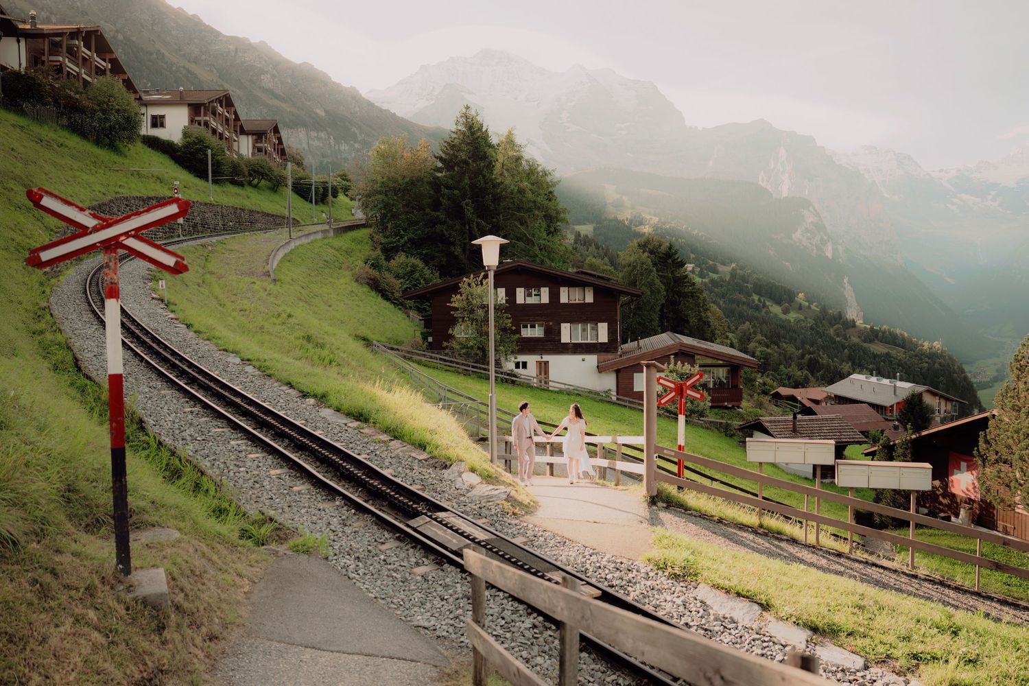 Scenic Swiss mountain railway track curves through a misty alpine village with traditional chalets and green hillsides.