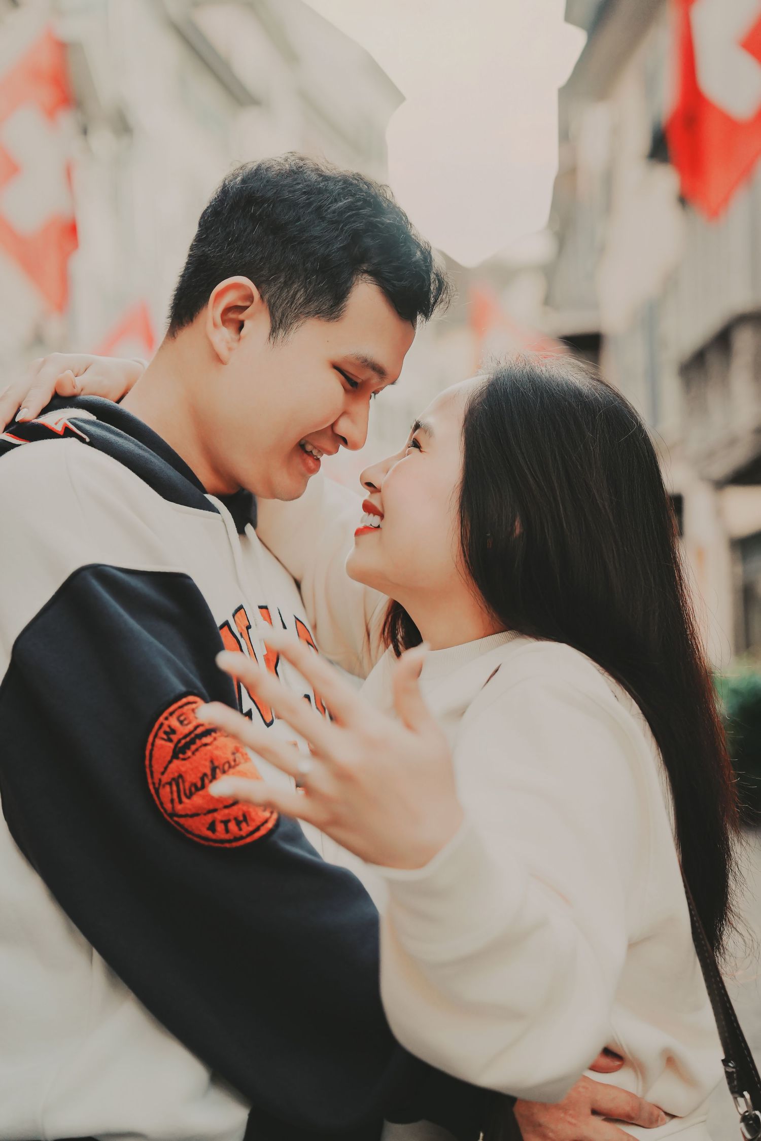 Young Asian couple embracing and smiling at each other on a European street with Swiss flags in background.
