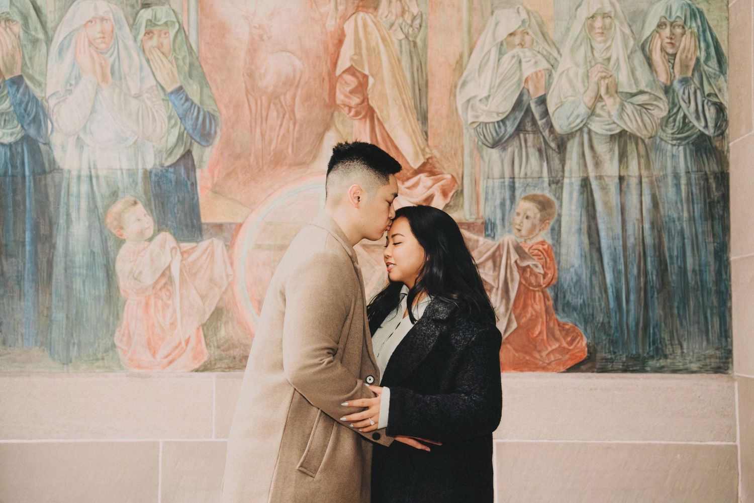 Engaged couple sharing an intimate moment in front of a colorful religious fresco mural.