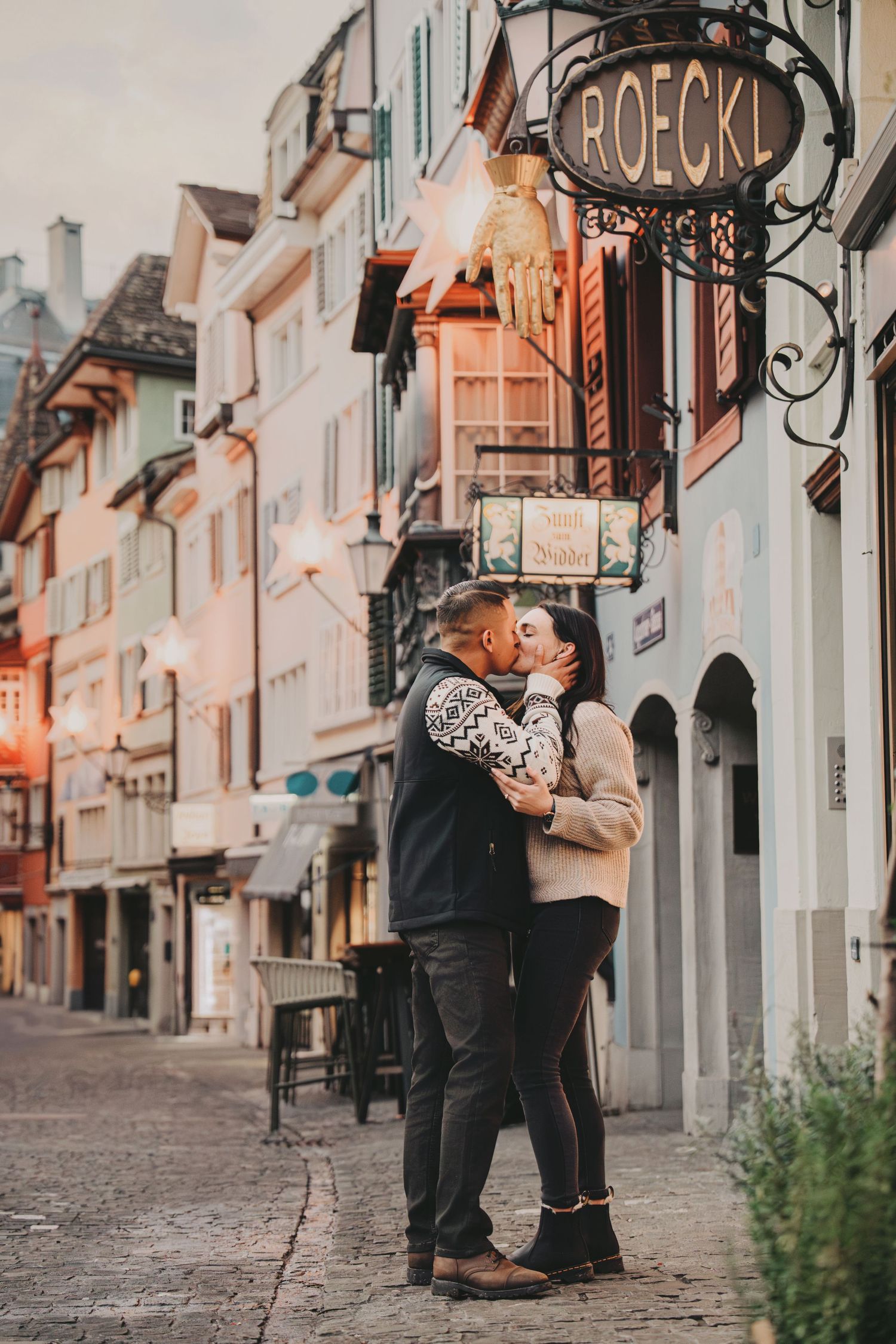 Couple sharing a romantic kiss on a cobblestone street in Zurich's old town near the Roeckl store.