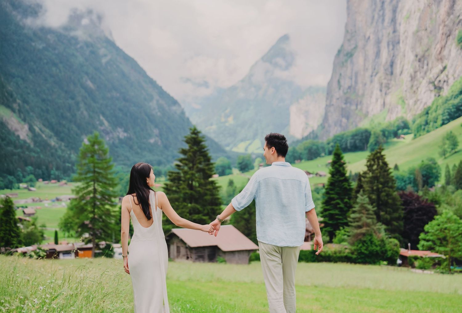 Couple holding hands in Lauterbrunnen valley Switzerland with mountains waterfall and green meadows backdrop.