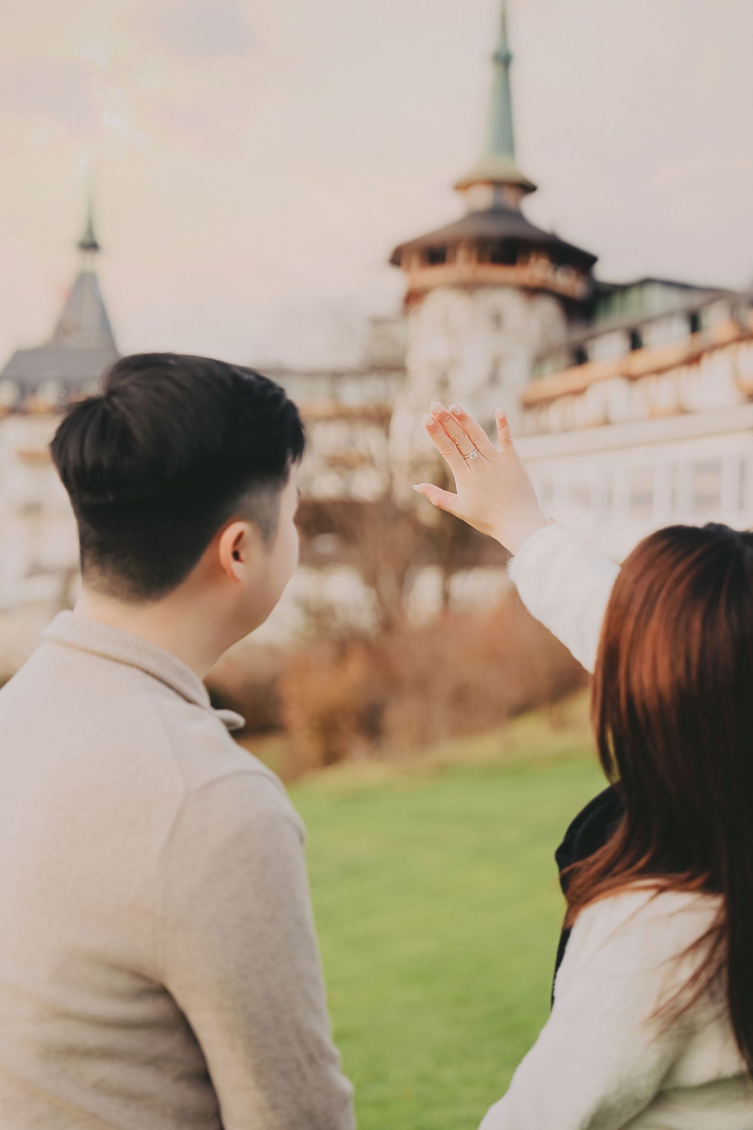Couple admiring European castle as woman shows off engagement ring outdoors.