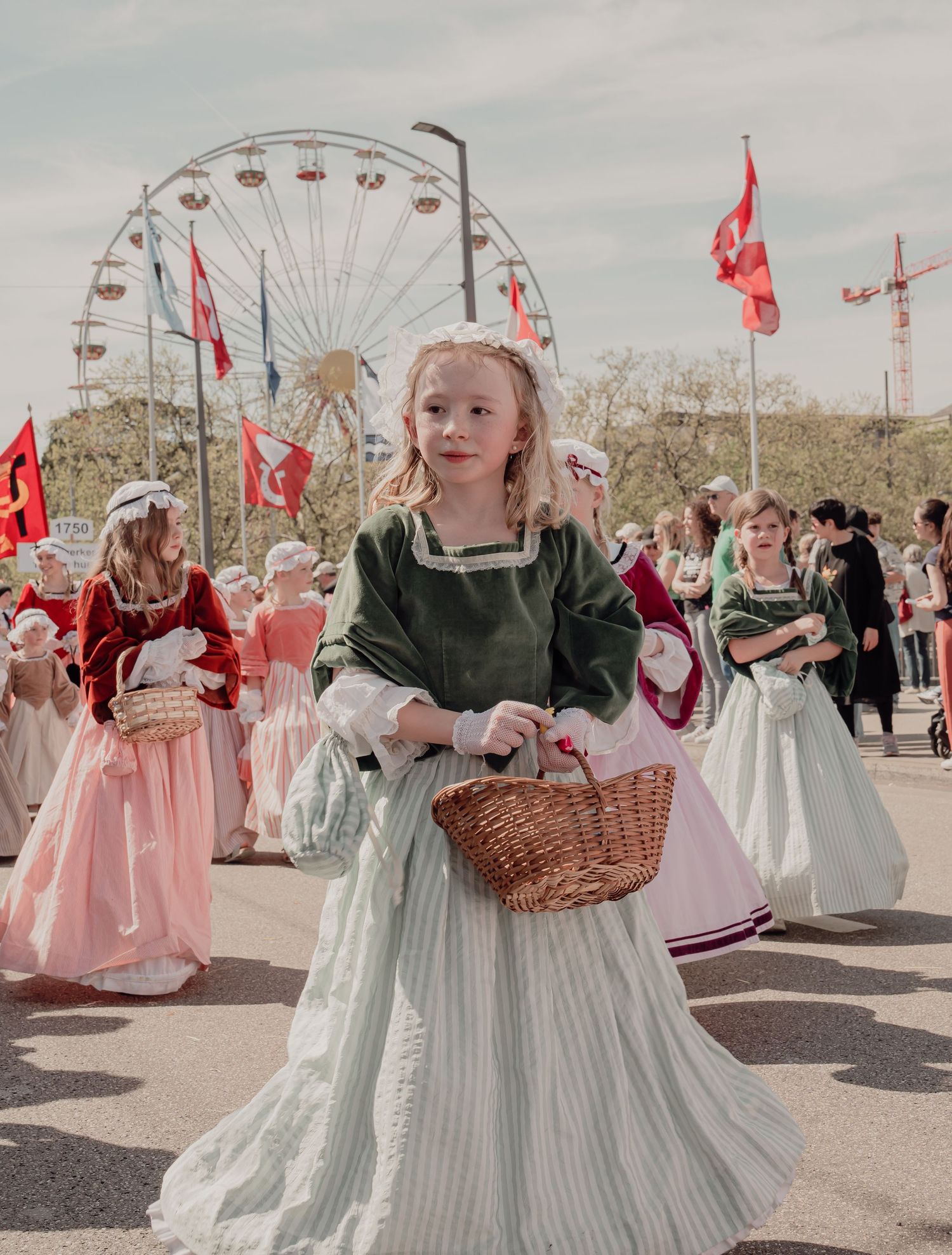 Blonde girl in green historical dress carrying a wicker basket at a traditional Swiss parade.