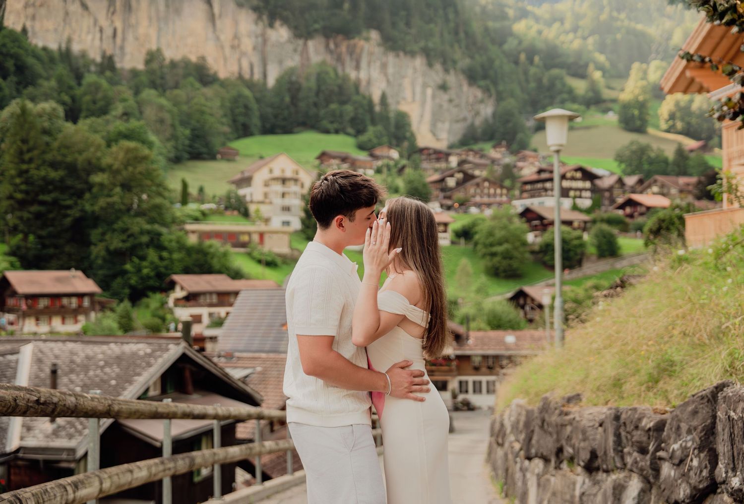 Couple sharing a kiss on a scenic overlook with Lauterbrunnen valley and Swiss village in background.