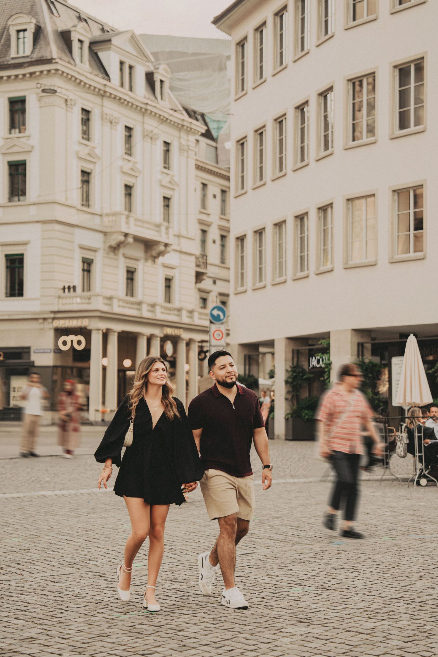 Young couple strolling through busy Zurich square surrounded by elegant European buildings.