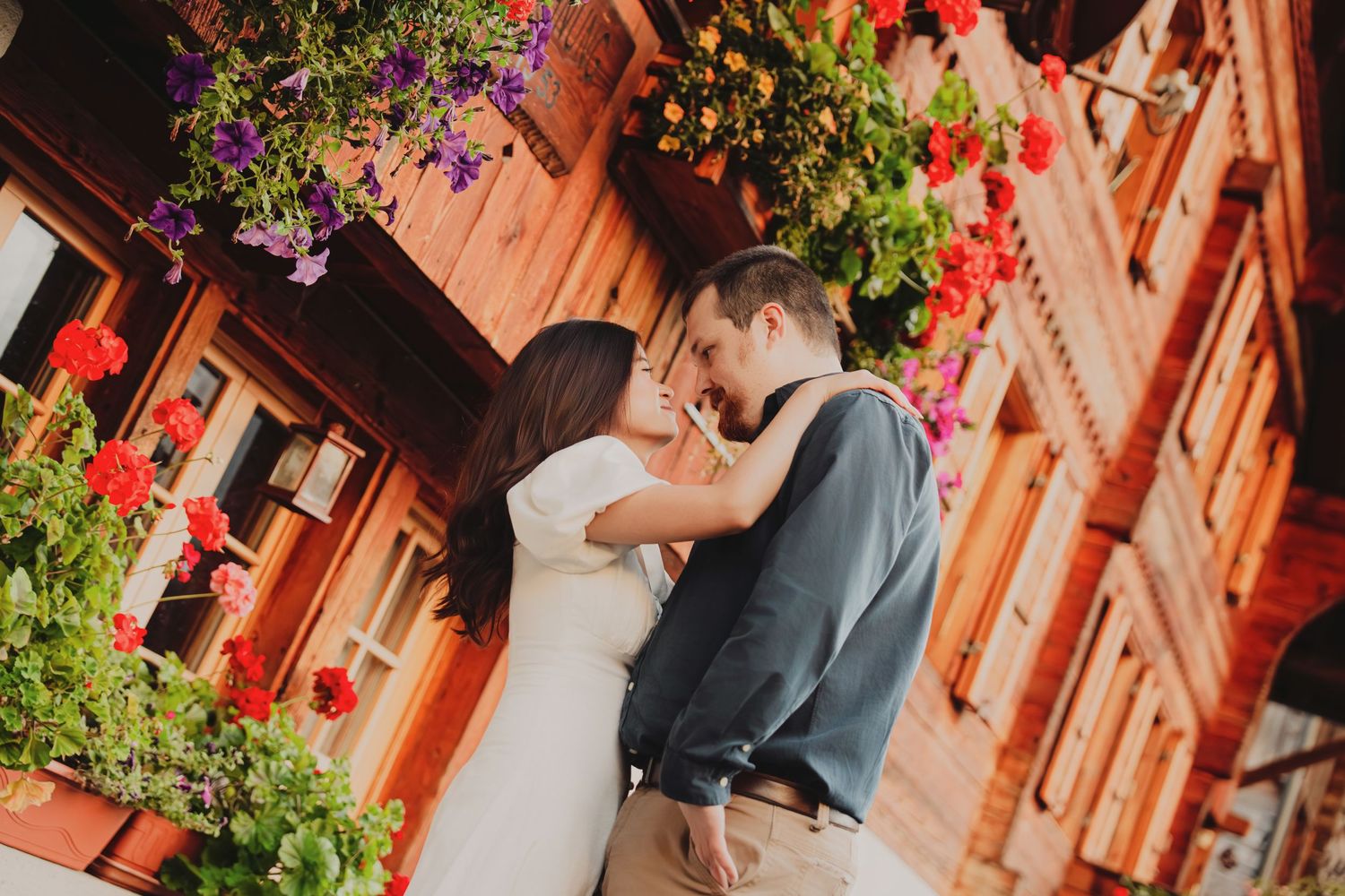 Romantic couple embracing under vibrant hanging flower boxes on a traditional Swiss building.