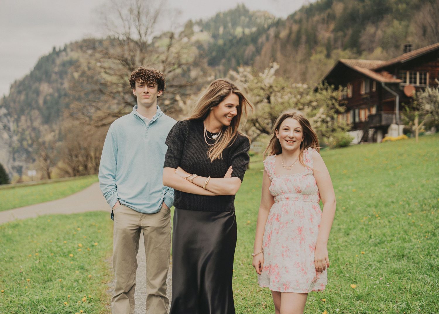 Mother with teenage son and daughter smiling together on green hillside in Swiss alpine setting.