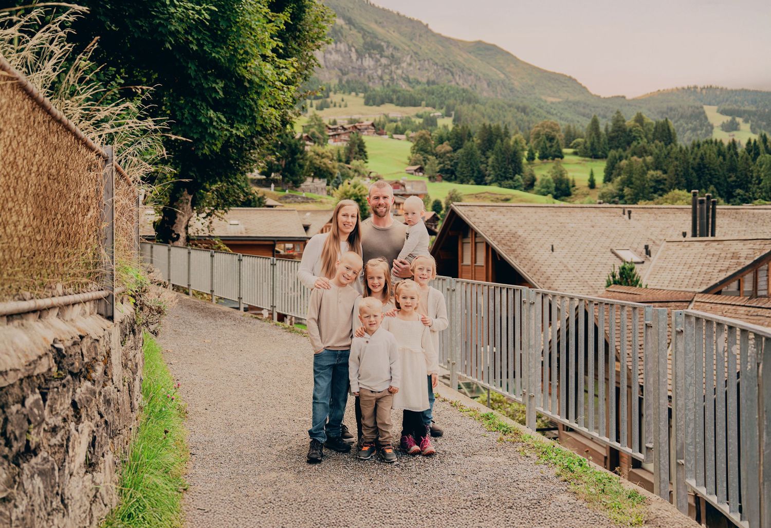 Family of parents and five young children posing on a scenic Swiss alpine village pathway.