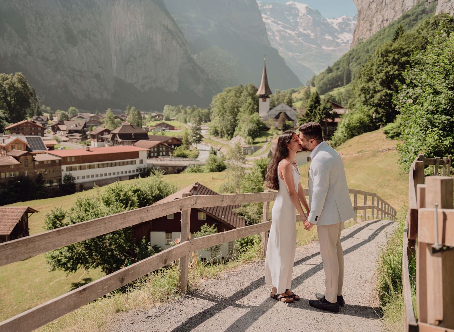 Bride and groom kissing on wooden bridge overlooking scenic Lauterbrunnen valley in Switzerland.