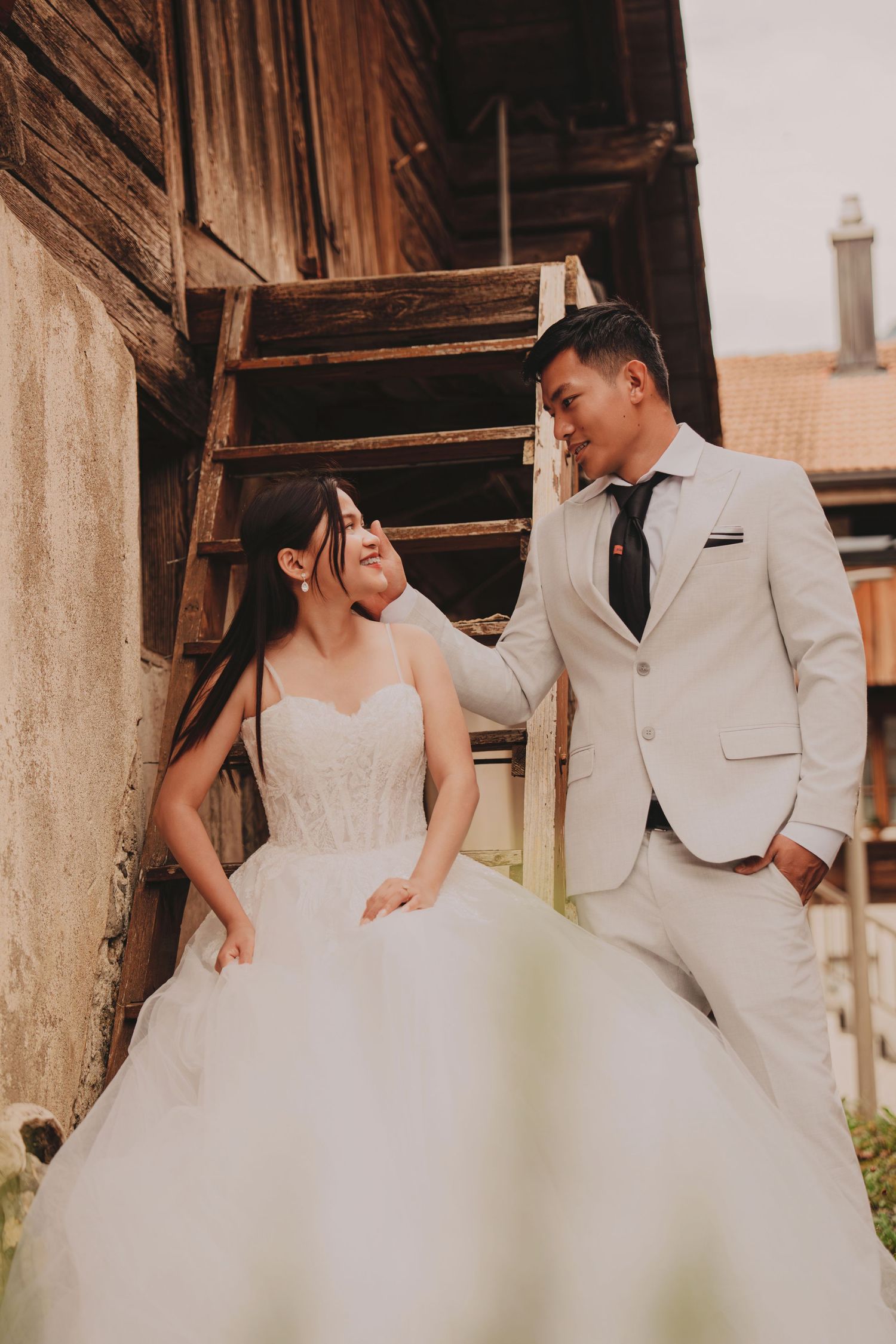 Bride and groom share a joyful moment gazing at each other near rustic wooden barn stairs.
