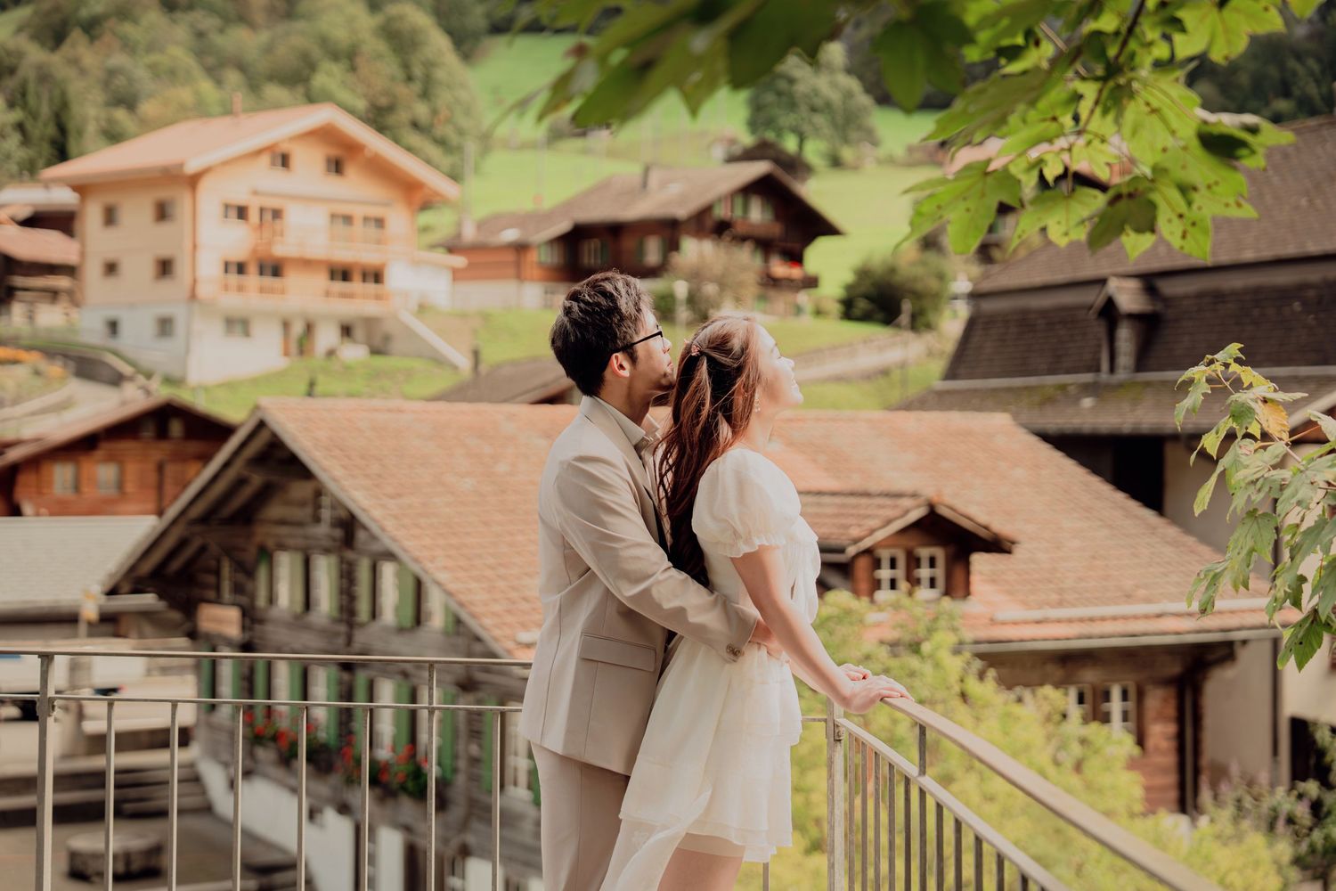 Couple kissing on a balcony with traditional Swiss chalet rooftops in the background.