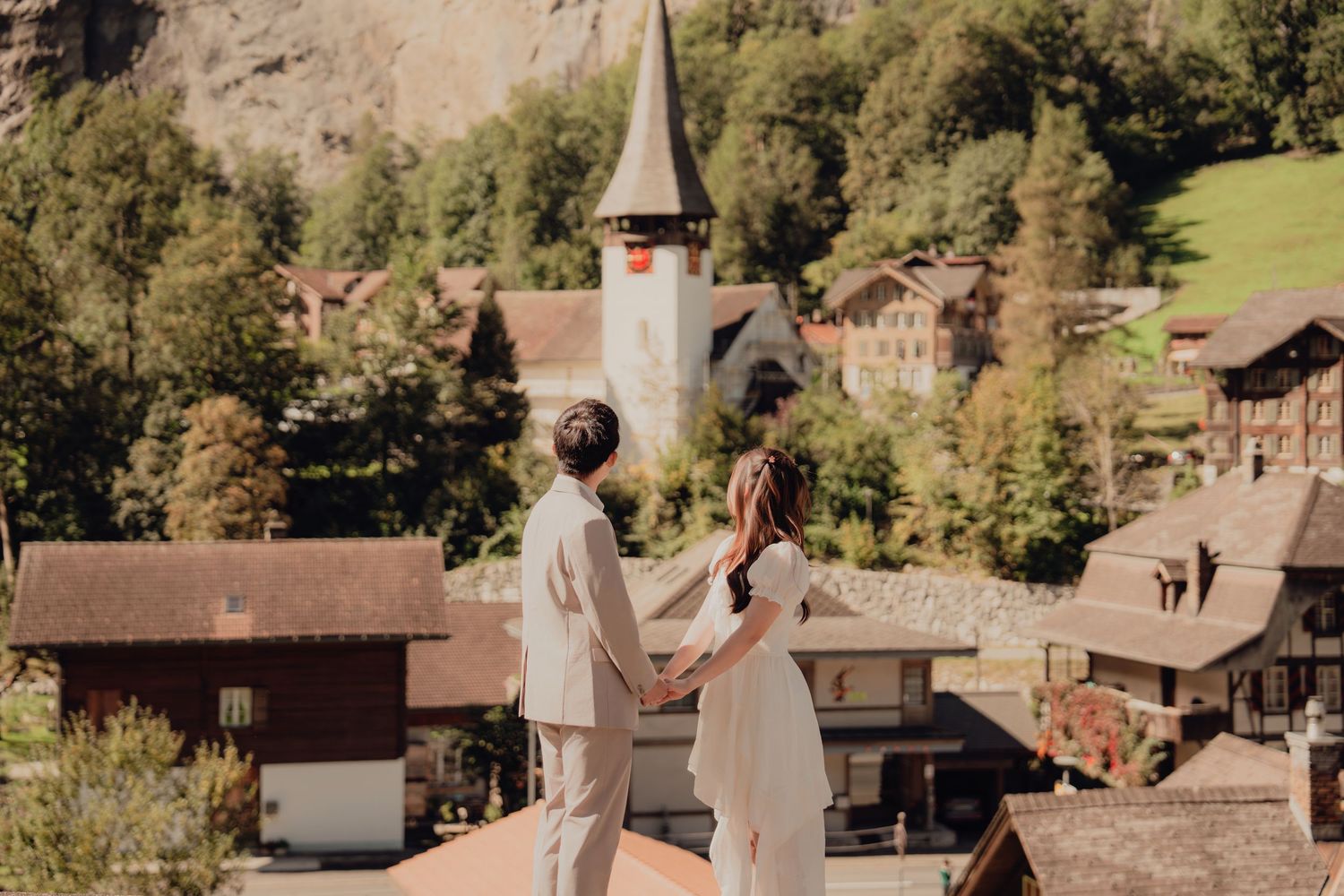 Couple holding hands overlooking a charming Swiss Alpine village with a historic church steeple.
