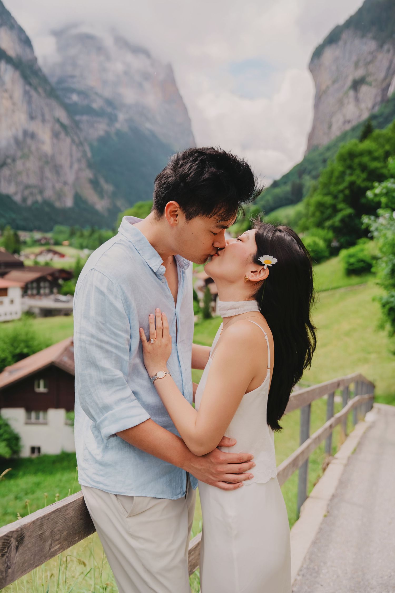 A couple shares a romantic kiss in Lauterbrunnen valley, Switzerland, with green meadows and dramatic cliffs in the background.