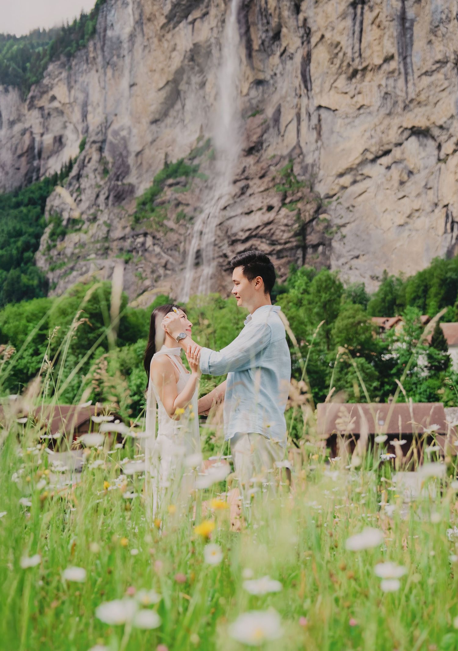 Couple dancing in a wildflower meadow with a stunning waterfall and rocky cliffs in Lauterbrunnen, Switzerland.