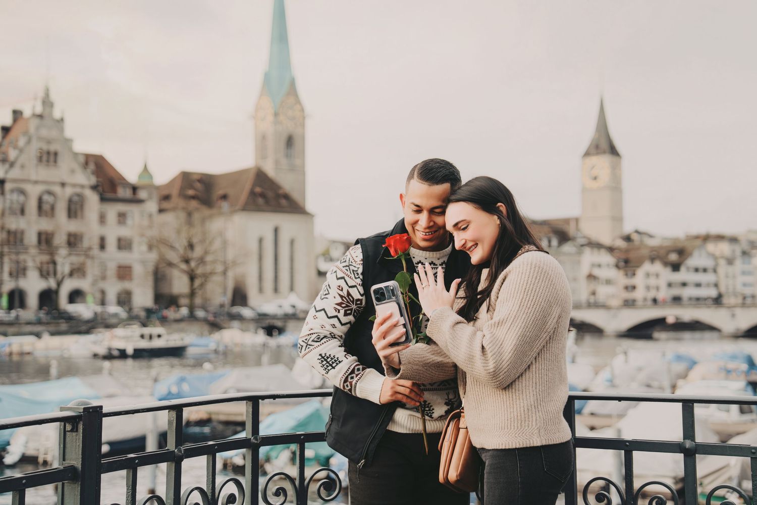 Happy couple viewing phone together near Zurich waterfront with church towers.