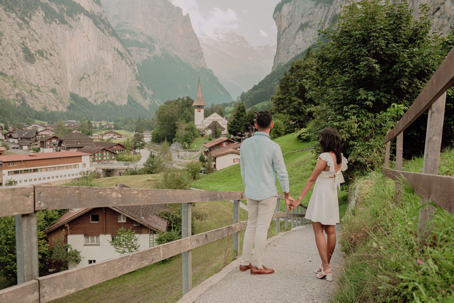 Couple walking hand in hand along a fence path overlooking the charming Lauterbrunnen village in Switzerland.