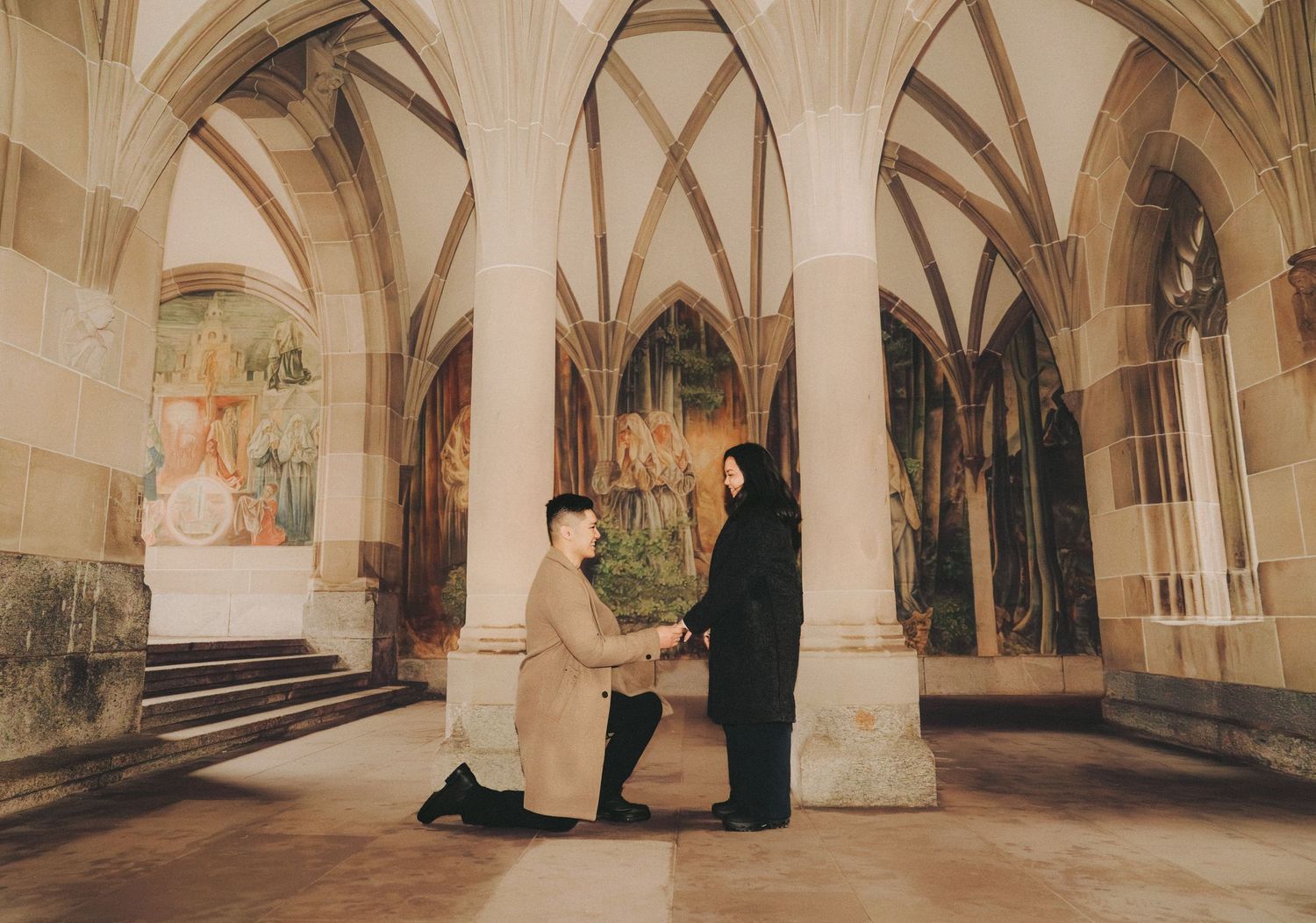 Man proposing on one knee to a woman inside a gothic cathedral with arched ceilings.