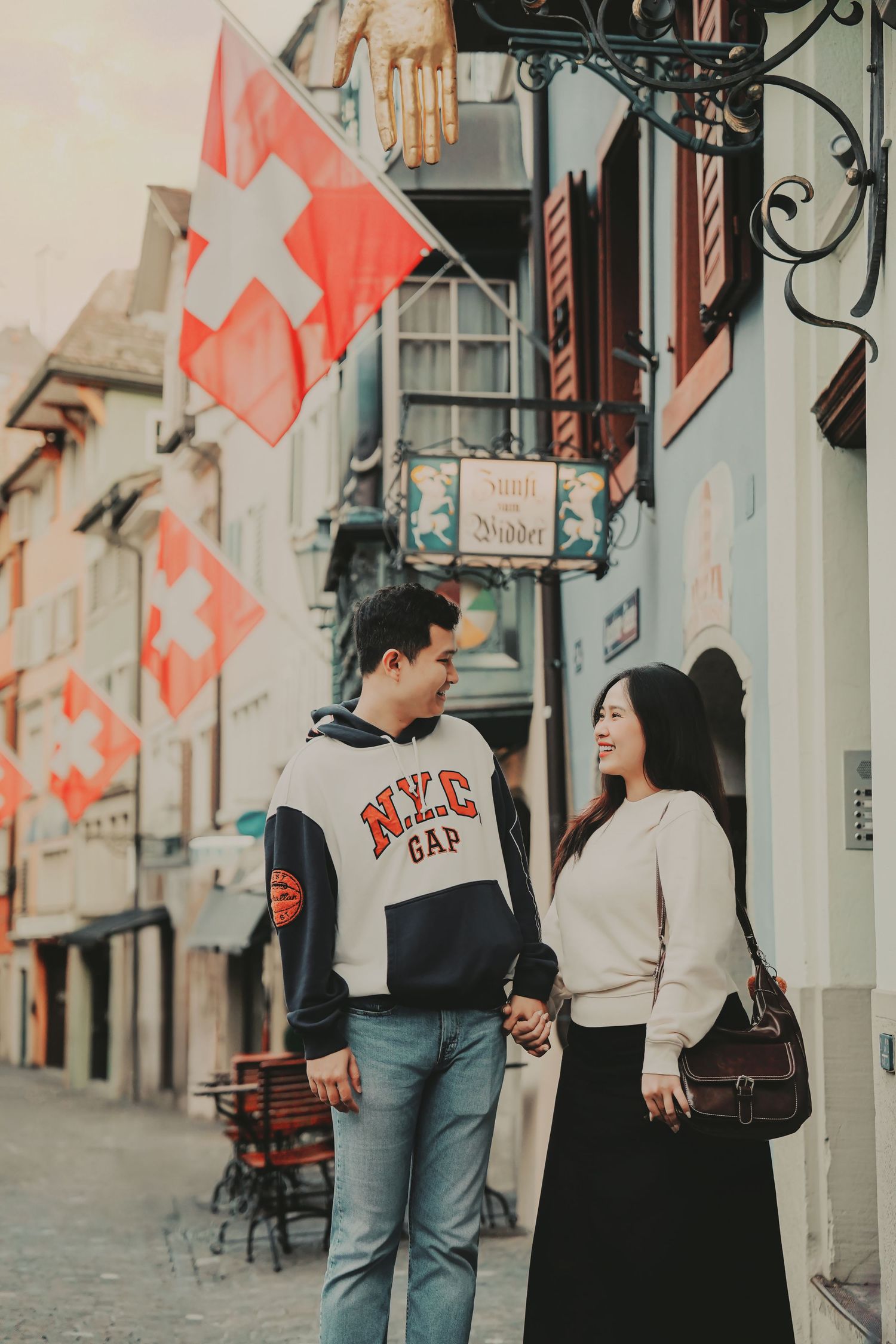 Couple walking hand in hand along a Zurich street lined with Swiss flags and traditional buildings.