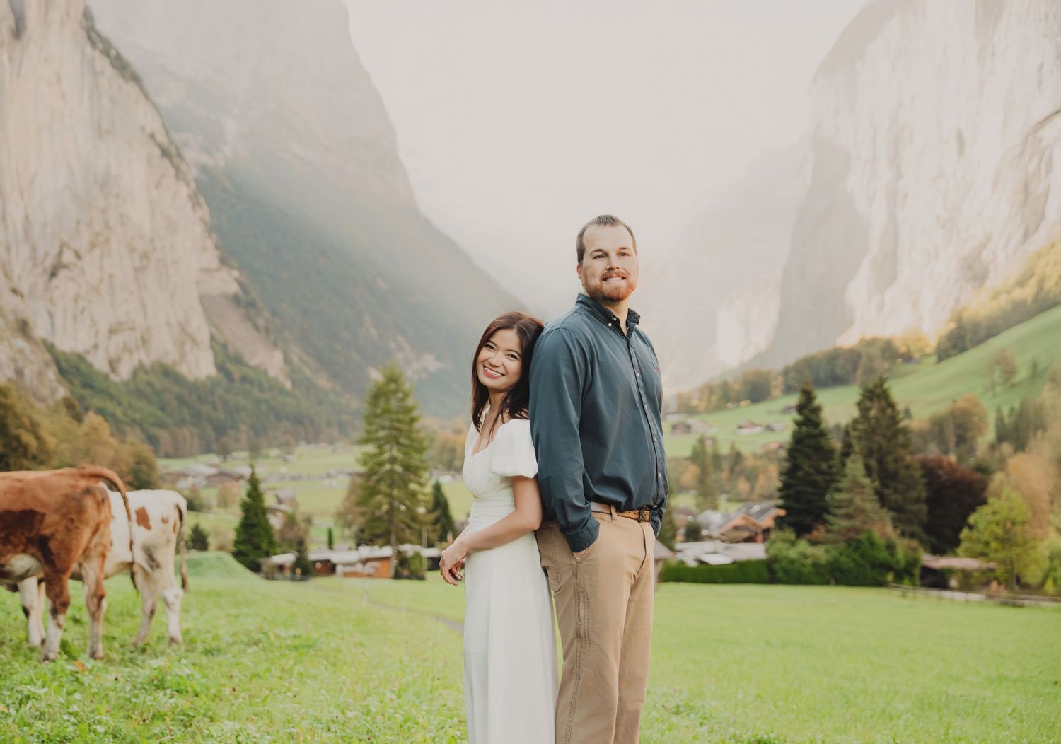 Couple standing back to back in a lush Swiss valley with grazing cows nearby.