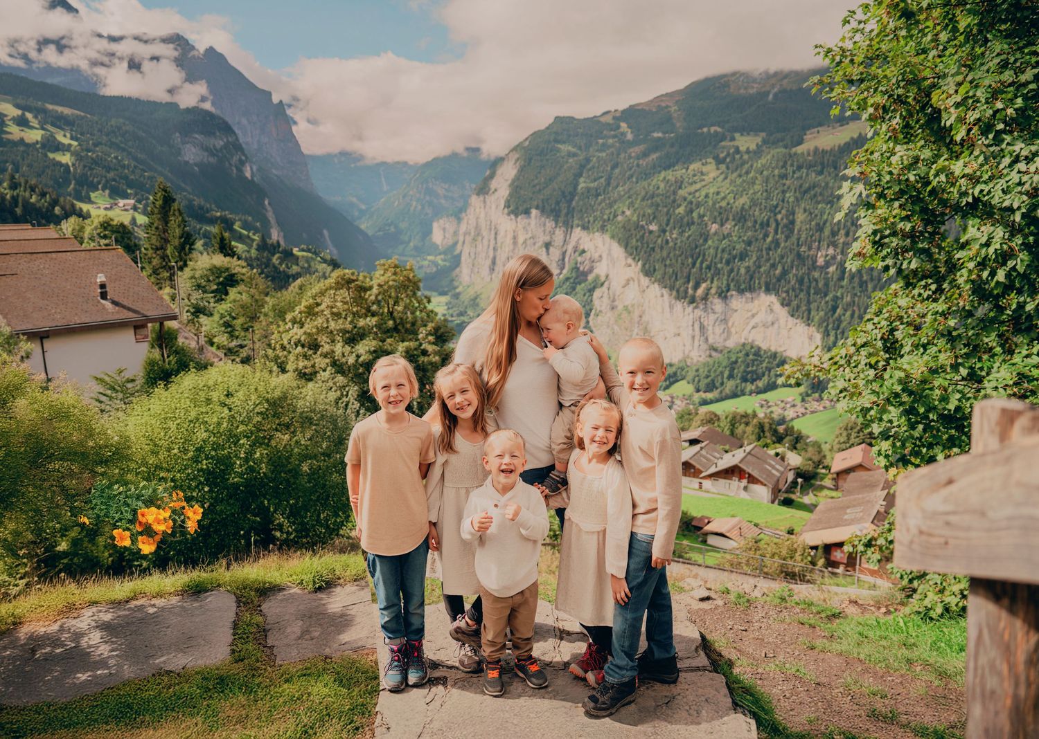 Family with six children posing together on stone steps with stunning Swiss Alpine valley and waterfall backdrop.