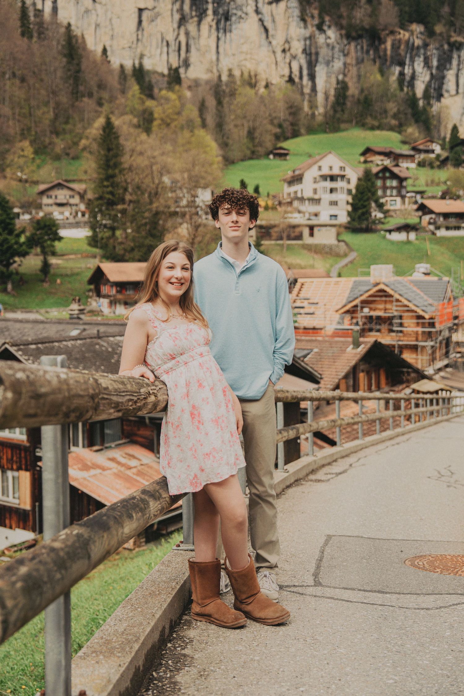 Couple standing together on a scenic bridge overlooking a charming Swiss mountain village with wooden chalets.