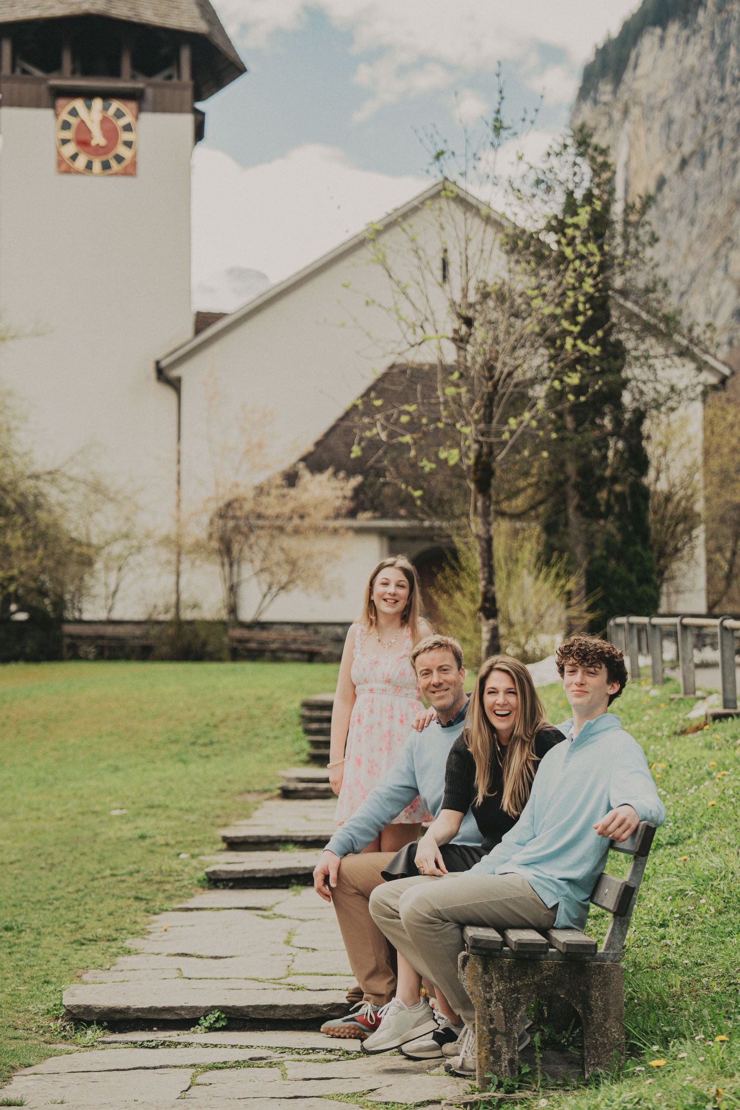 Family of four posing near a white Swiss church with a scenic mountain backdrop.