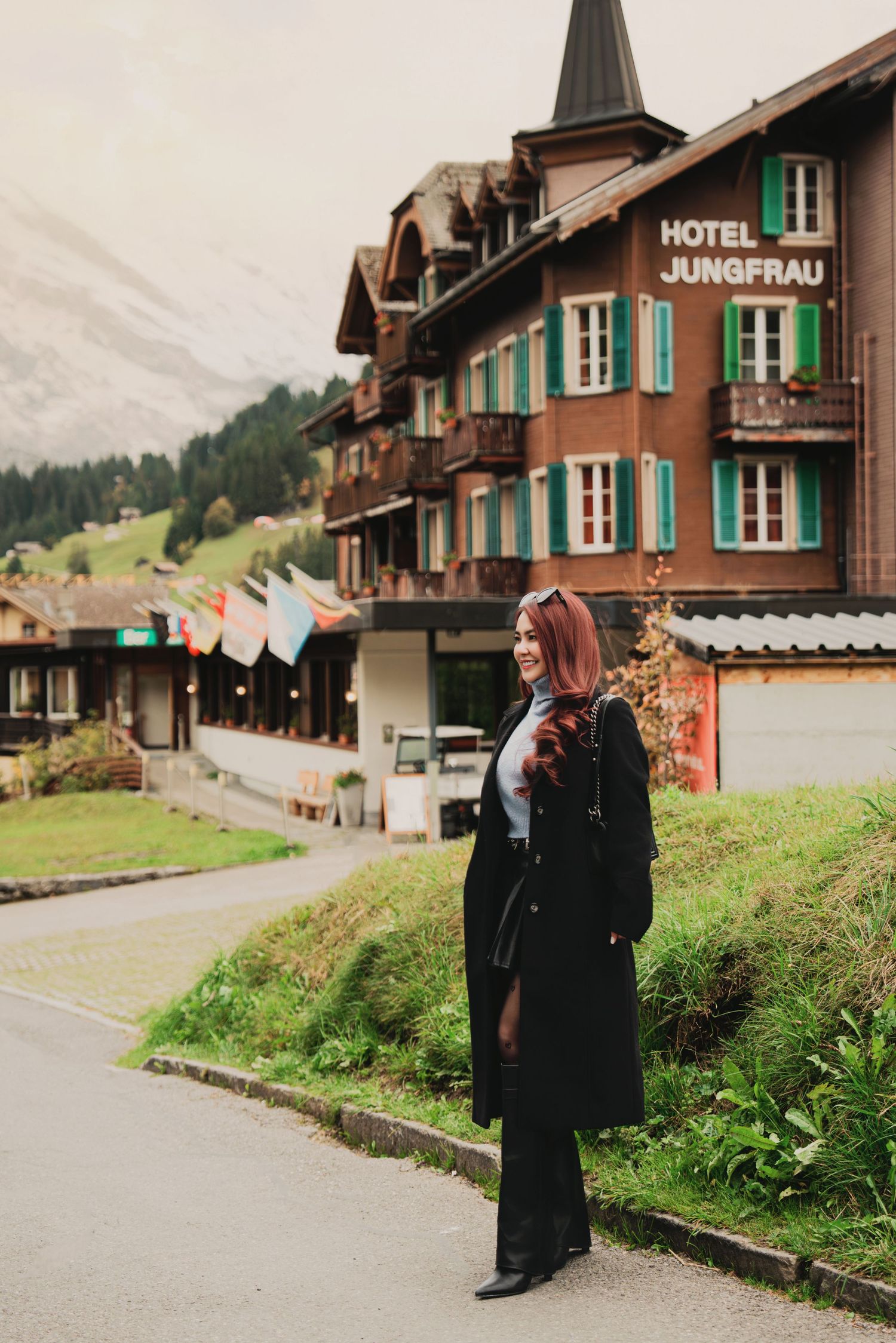 Woman in black coat stands before Hotel Jungfrau, a traditional Swiss chalet-style building in the Alps.
