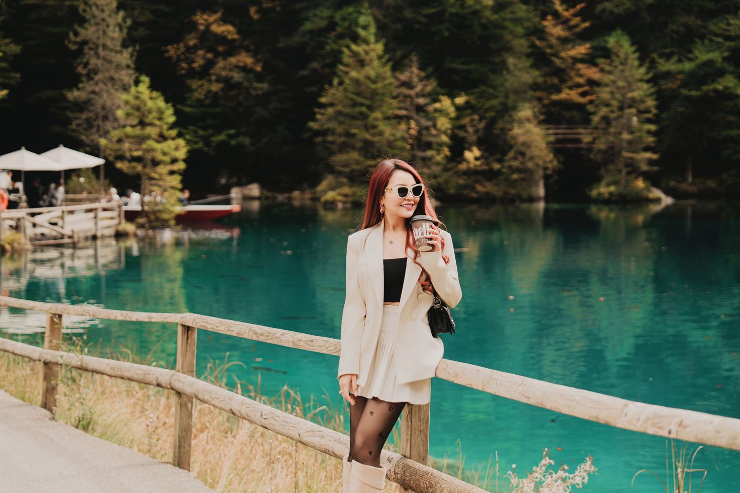 Fashionable woman with sunglasses holding coffee cup by stunning turquoise mountain lake.