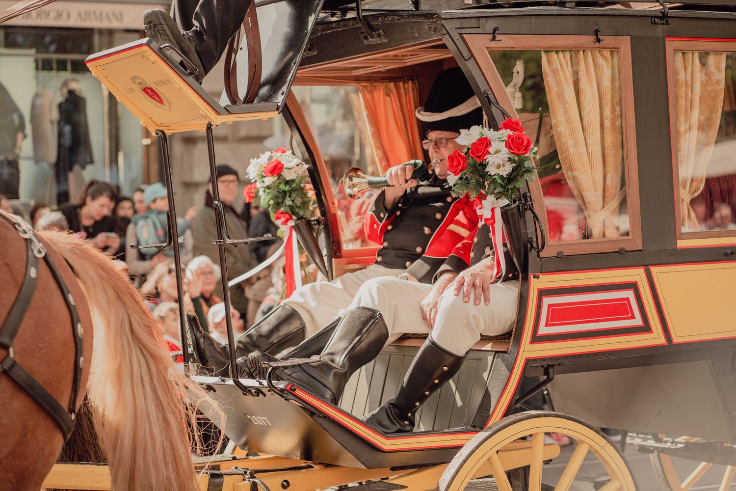 Uniformed coachman sits atop a horse-drawn carriage decorated with red and white roses during a city parade.