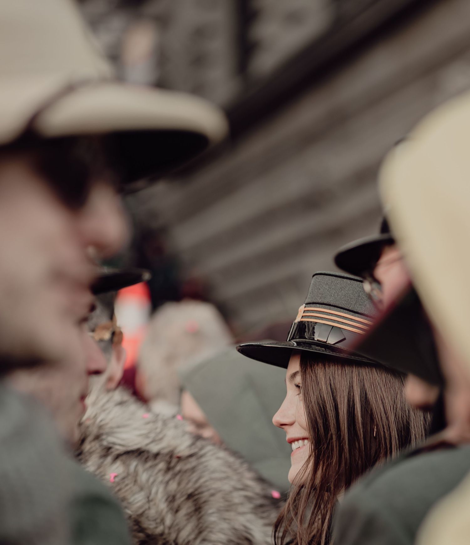 Young woman in a black hat smiling among a crowd of people wearing traditional hats at an event.