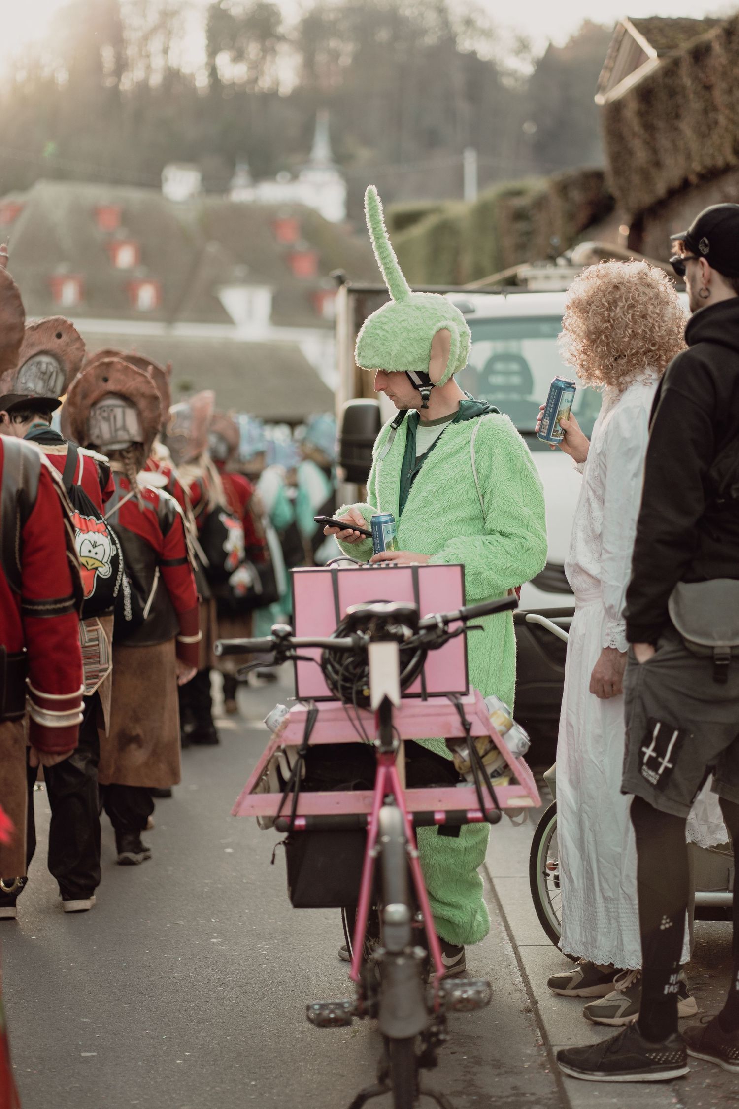 Person in green bunny costume at colorful carnival parade with pink cargo bike.
